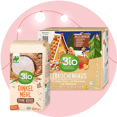 Eine Packung Dinkelmehl von dmBio neben einer Verpackung für ein Lebkuchenhaus-Bastelset mit weihnachtlichem Design und der Aufschrift „Das ist enthalten: Lebkuchenplatten, Zuckerguss, Dekorationsmaterial“