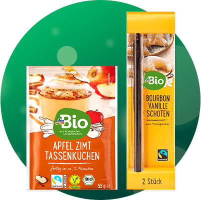 Zwei Bio-Produkte vor grünem Kreis: links orange Verpackung „dmBio Apfel Zimt Tassenkuchen“ 55 g mit Bild eines Tassenkuchens, rechts gelbe Verpackung „Bio Bourbon Vanille Schoten“ 2 Stück, Fairtrade-Siegel sichtbar