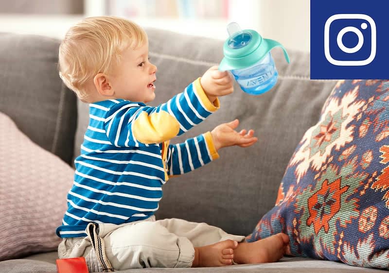 Kleinkind hält Trinkbecher auf Sofa