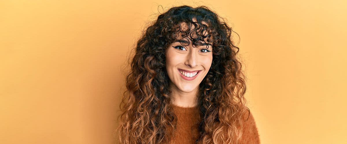 Frau mit lockigem Haar vor gelber Wand