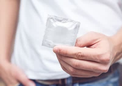 Eine männliche linke Hand hält ein verpacktes Kondom.