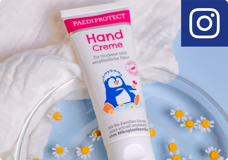 Eine Tube Paedi Protect Handcreme für trockene und empfindliche Haut liegt auf einem blauen Teller mit weißen Blüten.