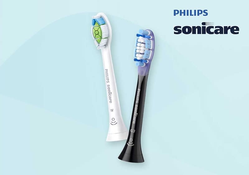 Zwei Philips Sonicare Zahnbürstenköpfe, einer in Weiß mit grünem Muster und einer in Schwarz mit blauen Borsten, vor einem hellblauen Hintergrund mit dem Philips Sonicare Logo