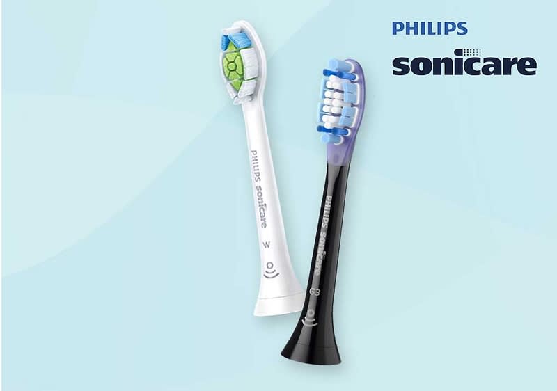 Zwei Zahnbürstenköpfe der Marke Philips Sonicare, einer in Weiß mit grünem und blauem Muster, der andere in Schwarz mit blauen Borsten, auf einem hellblauen Hintergrund