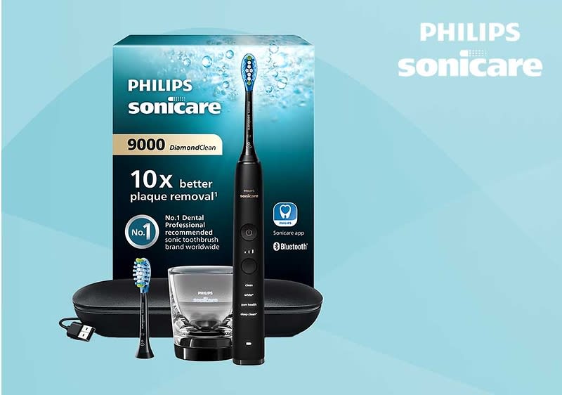 Schwarze Philips Sonicare 9000 Schallzahnbürste mit Ladestation, Ersatzbürstenkopf und Reiseetui vor der türkis-blauen Verpackung mit Aufschrift „Philips Sonicare 9000 DiamondClean“, Hinweis „10x better plaque removal“ und Bluetooth-Logo