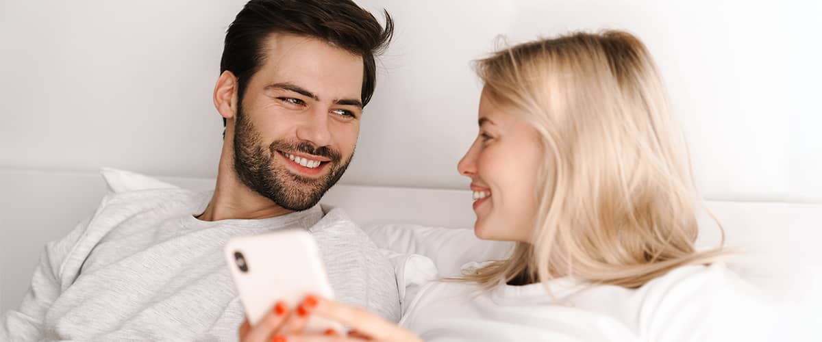 Paar zusammen im Bett rechnen den Eisprung am Smartphone aus
