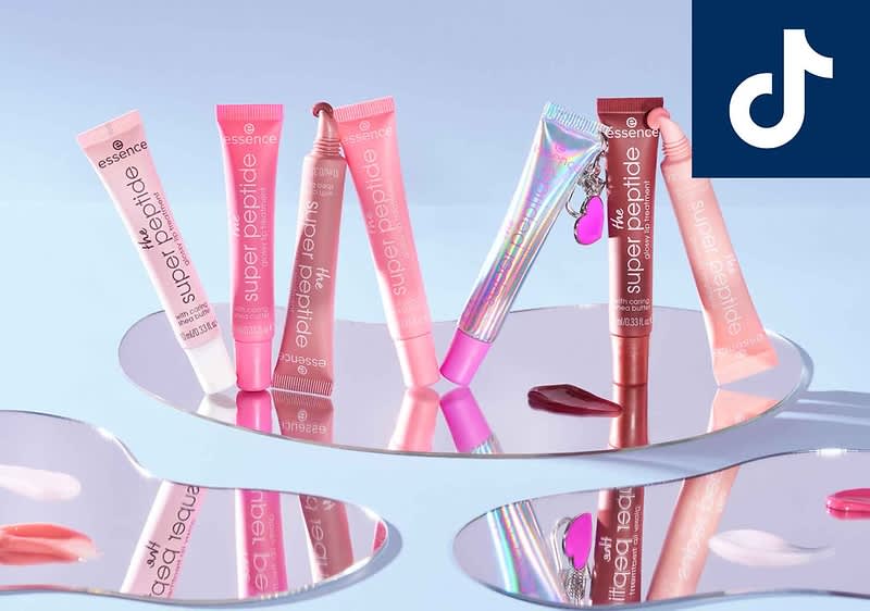 Mehrere Lipgloss-Tuben in verschiedenen Rosa- und Rottönen stehen auf einem Spiegel. Oben rechts ist das TikTok-Logo zu sehen.