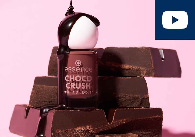 Ein Fläschchen essence Choco Crush Mini-Nagellack steht auf gestapelten Schokoladenstücken, mit schwarzer Flüssigkeit, die darüber fließt. Oben rechts ist ein YouTube-Symbol.