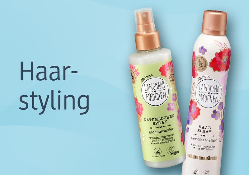 Zwei Stylingprodukte der Marke „Langhaar Mädchen“ auf blauem Hintergrund: links eine grünliche Sprühflasche mit Aufschrift „Naturlocken Spray“, rechts eine weiße Haarspray-Dose mit Blumendesign und Aufschrift „Hair Spray“, links daneben Schriftzug „Haarstyling“