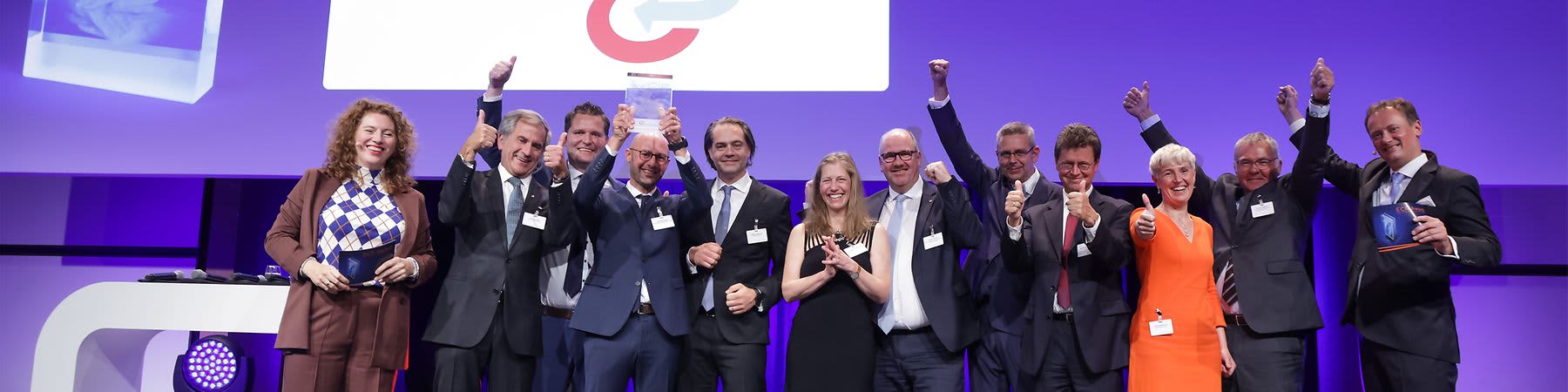 Eine Gruppe von Menschen steht auf einer Bühne und hält Trophäen in die Luft. Im Hintergrund ist der Schriftzug „Sustainability Excellence“ und ein Logo mit den Buchstaben „G“ und „C“ zu sehen.