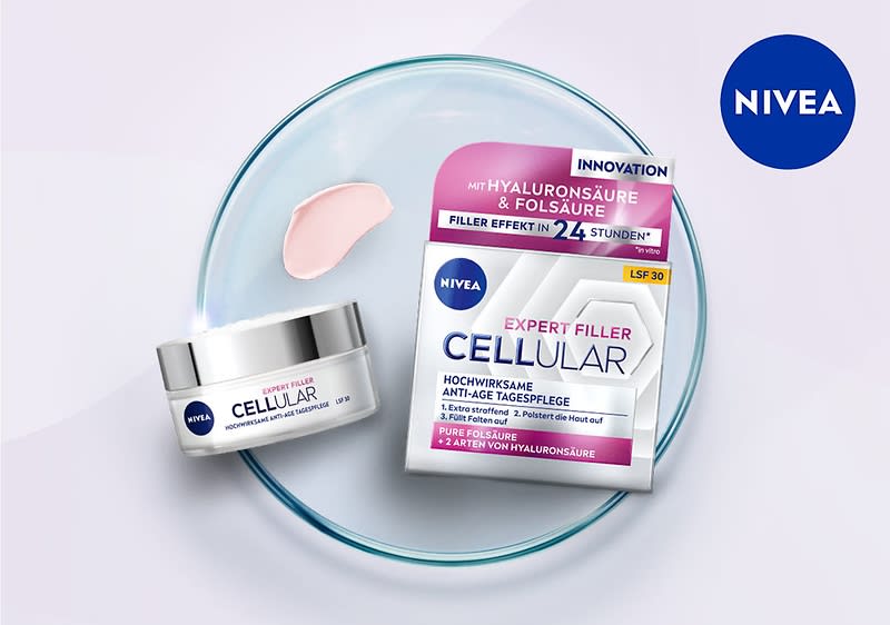 Eine Nivea Expert Filler Cellular Tagespflege mit Hyaluronsäure und Folsäure in einer weißen Dose und einer dazugehörigen Verpackung, die auf einem transparenten Teller liegt, daneben befindet sich ein rosafarbener Cremeklecks, oben rechts ist das Nivea-Logo in einem blauen Kreis zu sehen