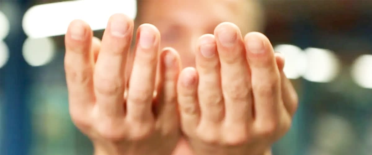 Zwei Hände mit leicht gebogenen Fingern sind im Vordergrund zu sehen, während der Hintergrund unscharf ist und eine Person im Hintergrund nur verschwommen erkennbar ist