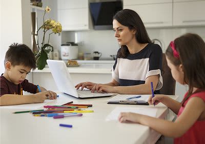  Mutter arbeitet am  Laptop während  Kinder malen