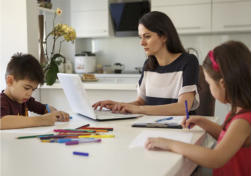 Mutter arbeitet am Laptop während Kinder malen