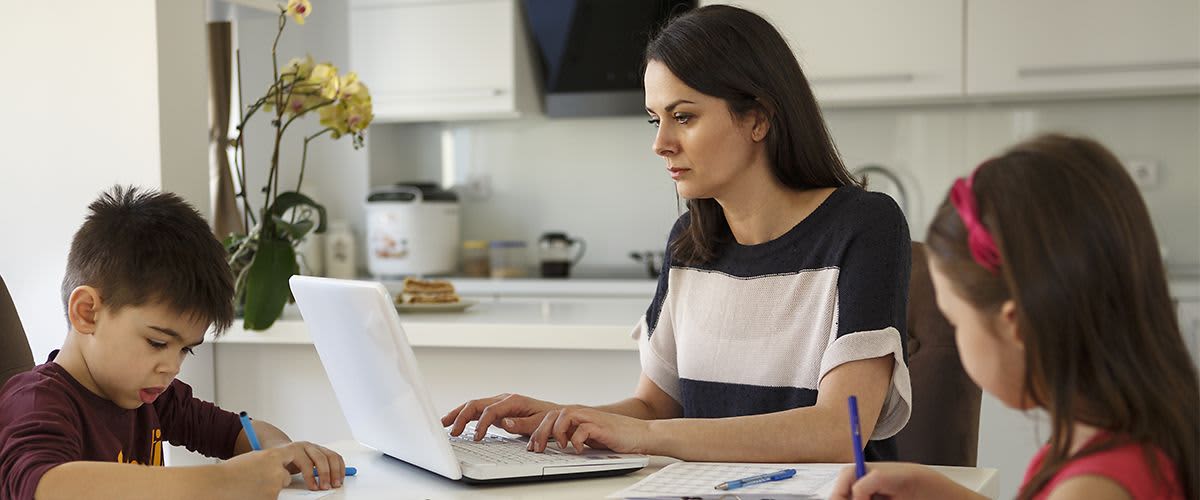  Mutter arbeitet am  Laptop während  Kinder malen