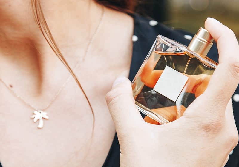 Frau sprüht Duft auf Dekolleté