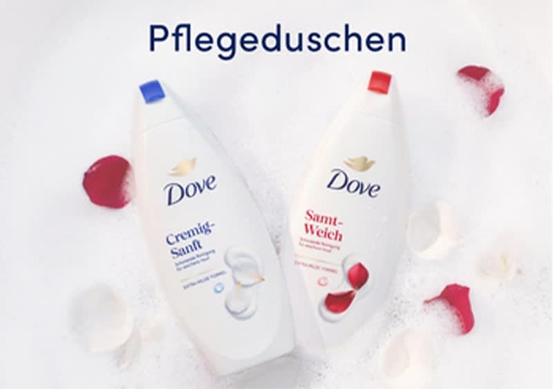 Zwei weiße Dove-Duschflaschen liegend auf Schaum; links Flasche mit blauem Verschluss und Aufschrift „Cremig-Sanft“, rechts Flasche mit rotem Verschluss und Aufschrift „Samt-Weich“, darüber Schrift „Pflegeduschen“, rote und weiße Rosenblätter rundherum