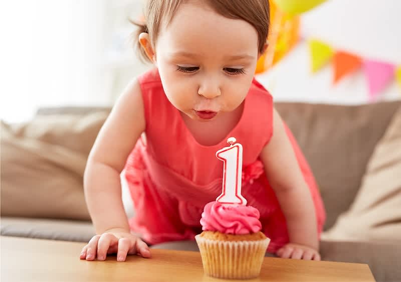 Kleinkind pustet Muffin mit Kerze zum 1. Geburtstag aus