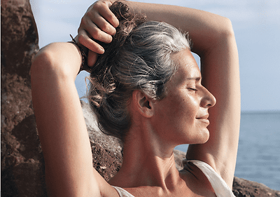 Frau steht mit Hände über dem Kopf am Meer und entspannt