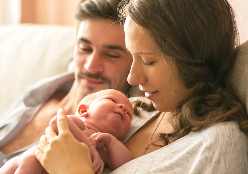 Junge Eltern mit Neugeborenem im Wochenbett