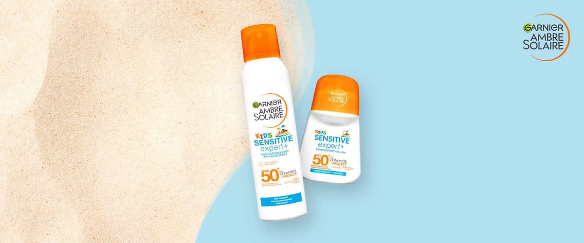 Zwei Garnier Ambre Solaire Sonnenschutzprodukte für Kinder: links weiß-orange Spraydose mit Aufschrift „Kids Sensitive expert+ SPF 50“, rechts weiße-orange Lotionflasche mit gleicher Beschriftung, auf hellblauem Hintergrund und Garnier-Logo oben rechts