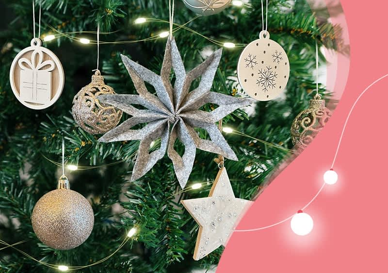 Ein geschmückter Weihnachtsbaum mit silbernen und goldenen Kugeln, einem großen silbernen Stern und verschiedenen hölzernen Ornamenten, darunter ein Geschenk, ein Stern und ein ovales Ornament mit Schneeflockenmuster