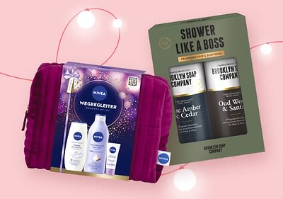 Zwei Geschenksets vor einem rosa Hintergrund, links ein Nivea-Set mit lila Verpackung und den Produkten Wegbegleiter, rechts ein Brooklyn Soap Company Set mit schwarzer Verpackung und den Duschgels Blue Amber & Cedar sowie Oud Wood & Sandalwood