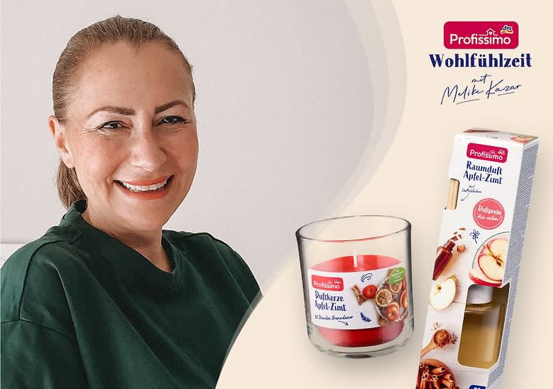 Eine rote Duftkerze im Glas mit der Aufschrift „Duftkerze Apfel-Zimt“ neben einer Produktverpackung mit der Aufschrift „Raumduft Apfel-Zimt“ und dem Profissimo-Logo, im Hintergrund Lichterkette und Schriftzug „Wohlfühlzeit mit Milka Kraw“