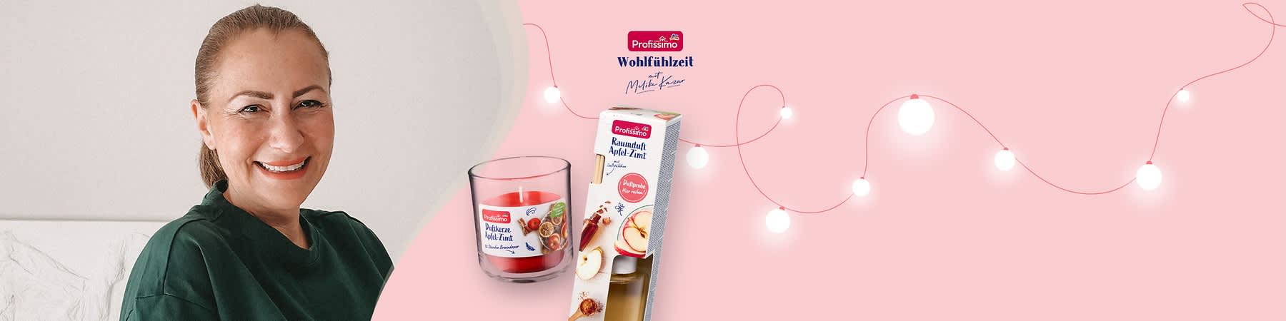 Eine rote Duftkerze im Glas mit der Aufschrift „Duftkerze Apfel-Zimt“ neben einer Verpackung mit der Aufschrift „Profissimo Raumduft Apfel-Zimt“ und Bildern von Äpfeln und Zimtstangen, im Hintergrund eine Lichterkette und das Profissimo-Logo mit dem Text „Wohlfühlzeit mit Melike Kara“