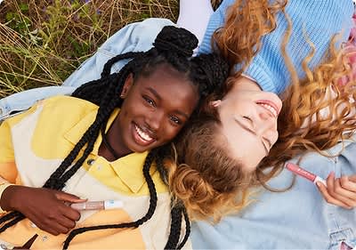 Zwei Frauen liegen Kopf an Kopf auf einer Wiese.