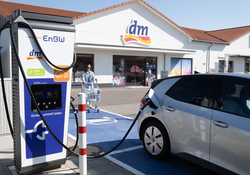 Ein E-Auto lädt an einer Schnellladesäule der EnBW vor einem dm-Markt. Die Sonne scheint.