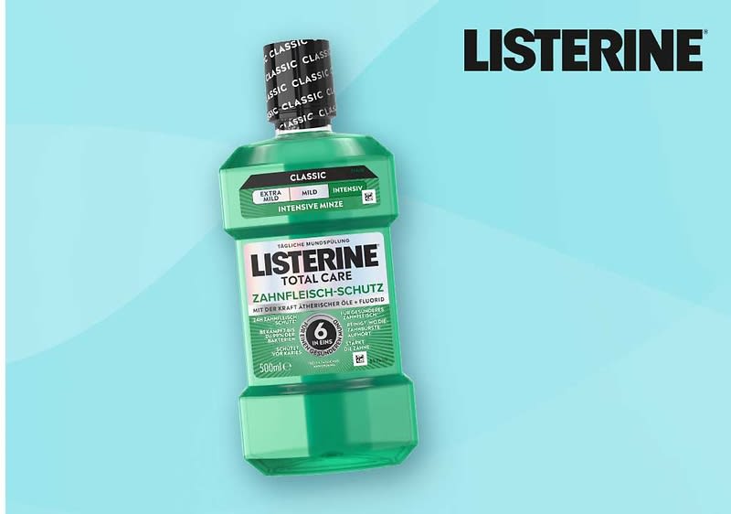 Grüne Flasche LISTERINE Mundspülung „Total Care Zahnfleisch-Schutz“ mit schwarzem Schraubverschluss und sichtbarer Aufschrift „6-fach Schutz“ vor hellblauem Hintergrund