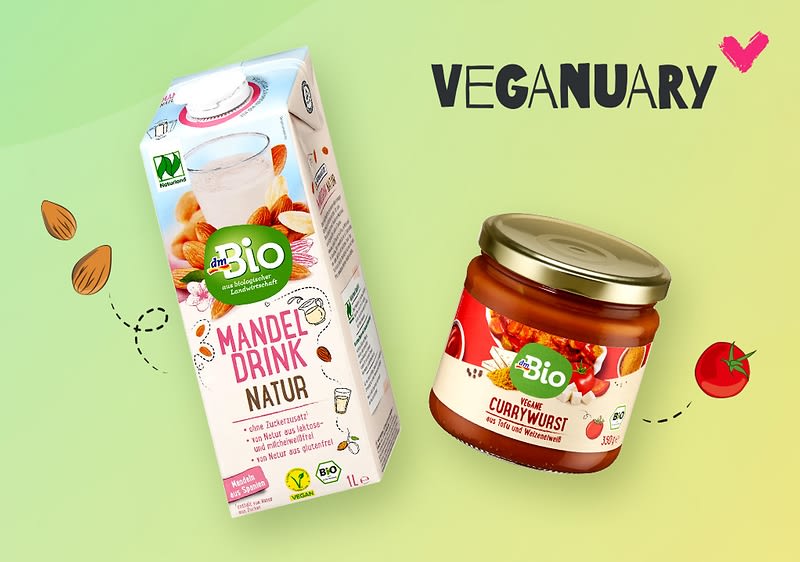 Eine Verpackung von „Bio Mandel Drink Natur“ neben einem Glas „Bio Vegane Currywurst“ auf einem hellgrünen Hintergrund mit dem Schriftzug „Veganuary“ und einem rosa Herz.