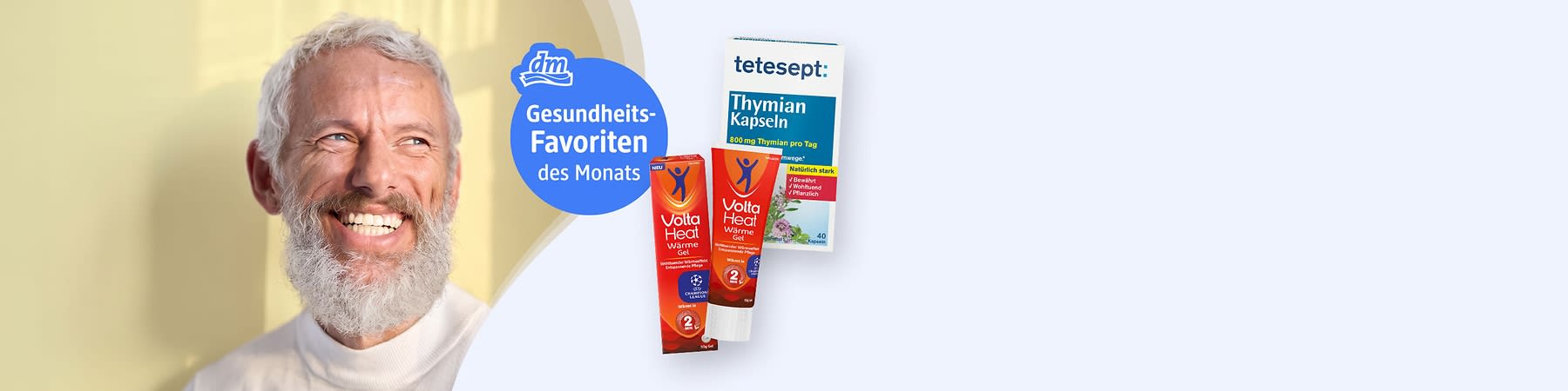 Älterer Mann mit weißem Bart lächelt nach rechts; daneben blauer runder Schriftkreis mit dm-Logo und Text „Gesundheits-Favoriten des Monats“ sowie zwei Tuben Volta Heat Wärmegel in roter Verpackung und eine Packung tetesept Thymian Kapseln sichtbar