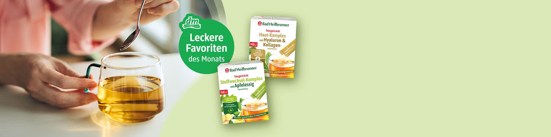 Hand mit Teelöffel über einer Glastasse mit hellem Aufguss; grüner Kreis mit dm-Logo und weißer Schrift „Leckere Favoriten des Monats“; zwei Packungen Bad Heilbrunner Teetrinkerzeugnisse, vorn „Stoffwechsel-Komplex mit Apfelessig“, hinten „Haut-Komplex mit Hyaluron & Kollagen“