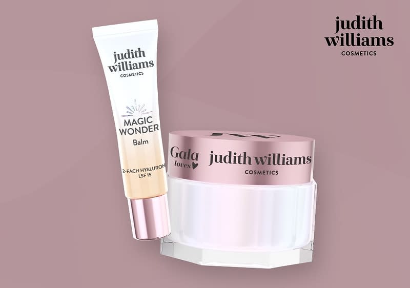 Eine Produktverpackung mit einem weißen Tube-Balm mit der Aufschrift „Magic Wonder Balm 2-fach Hyaluron Lift“ und einem rosafarbenen Deckel, daneben ein rosafarbenes Tiegel mit der Aufschrift „Gala Secrets judith williams cosmetics“, im Hintergrund der Text „judith williams cosmetics“