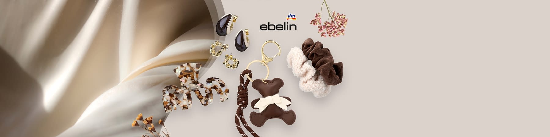 Mehrere Haarschmuckstücke auf hellem Hintergrund: eine große perlmuttfarbene Haarspange mit geklammertem Design rechts, links eine cremefarbene, blütenförmige Haarklammer, oben zwei goldfarbene Creolen und zwei kleine transparente Blüten-Haarspangen mit roségoldenen Akzenten, außerdem zwei quadratische Aufkleber mit Blumenmotiven; rechts oben das Markenlogo ebelin ohne Punkt am Satzende