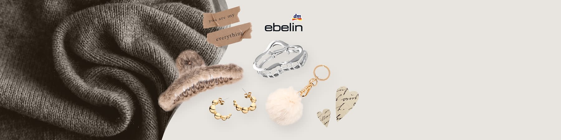 Eine Collage mit einem grauen Strickschal, einer silbernen Haarspange, einer braunen Haarspange mit Fell, goldenen Ohrringen, einem Schlüsselanhänger mit weißem Fellball, zwei Papierherzen mit Schrift und einem Papierstreifen mit der Aufschrift „you are my everything“ sowie dem ebelin-Logo