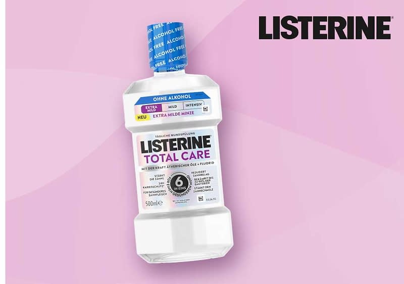 Weiße Flasche Mundspülung LISTERINE Total Care, Aufschrift „OHNE ALKOHOL“, „EXTRA MILDE MINZE“, 500 ml, pinker Hintergrund, LISTERINE-Logo oben rechts