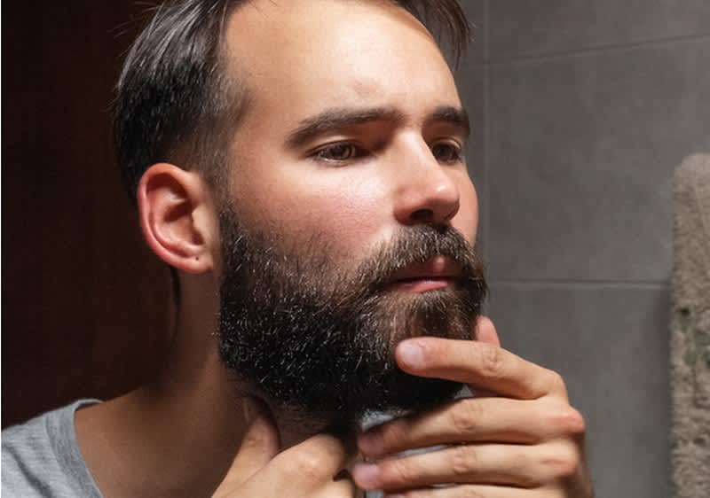 Mann betrachtet seinen Bart