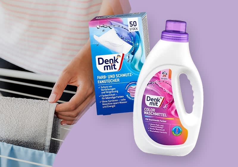 Eine Hand legt ein weißes Tuch auf einen Wäscheständer, daneben eine Packung Denkmit Farb- und Schmutzfangtücher mit blauer und pinker Gestaltung und der Aufschrift „50 Stück“, sowie eine weiße Flasche Denkmit Color Waschmittel mit pinkem Etikett und lila Verschluss