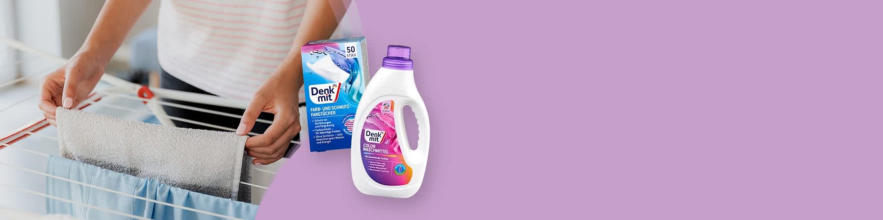 Eine Hand legt ein weißes Tuch auf einen Wäscheständer, daneben eine Packung Denkmit Farb- und Schmutzfangtücher mit blauer und pinker Gestaltung und der Aufschrift „50 Stück“, sowie eine weiße Flasche Denkmit Color Waschmittel mit pinkem Etikett und lila Verschluss