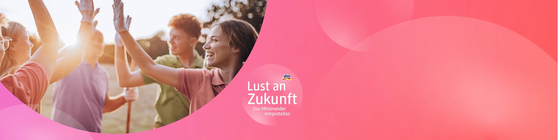 Drei Personen stehen im Freien und tragen Gartenhandschuhe, während sie sich gegenseitig abklatschen, im Hintergrund sind Bäume und eine Wiese zu sehen, auf der rechten Seite des Bildes befindet sich ein rosa Bereich mit dem Text Lust an Zukunft - Das Miteinander mitgestalten und dem dm-Logo.
