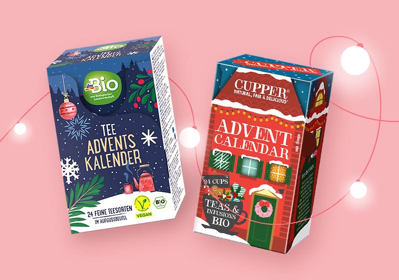 Zwei Produktverpackungen von Tee-Adventskalendern vor einem rosa Hintergrund mit weißen Lichtpunkten, links eine dunkelblaue Verpackung mit grünen und roten Weihnachtsmotiven, Aufschrift: Bio Tee Advents Kalender, 24 feine Teesorten, Vegan, rechts eine rot-grüne Verpackung mit einem Hausmotiv und der Aufschrift: Cupper Natural, Fair & Delicious Advent Calendar, 24 Cups Teas & Infusions Bio