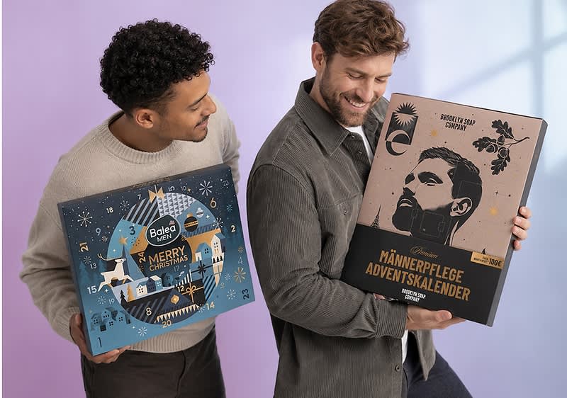 Zwei Männer halten Adventskalender; links ein blauer Balea Men Adventskalender mit Winterlandschaft und der Aufschrift „Merry Christmas“, rechts ein brauner „Männerpflege Adventskalender“ mit stilisiertem Männerporträt und Text „Brooklyn Soap Company“