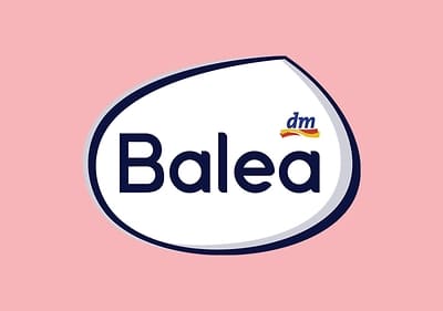 Das Bild zeigt ein ovales Logo mit einem weißen Hintergrund und einem dunkelblauen Rand, auf dem in großer dunkelblauer Schrift das Wort Balea steht, darüber befindet sich das dm-Logo mit einem kleinen blauen Schriftzug und einem gelb-roten Bogen, der Hintergrund des Bildes ist rosa.
