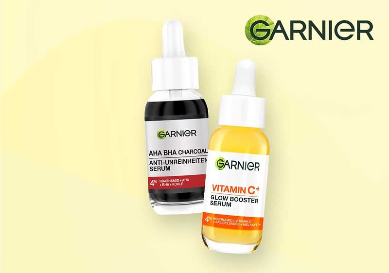 Zwei Garnier-Serumfläschchen mit Pipetten: links schwarzes Fläschchen mit Aufschrift „AHA BHA CHARCOAL ANTI-UNREINHEITEN SERUM“, rechts gelbes Fläschchen mit Aufschrift „VITAMIN C+ GLOW BOOSTER SERUM“, oben rechts Garnier-Logo