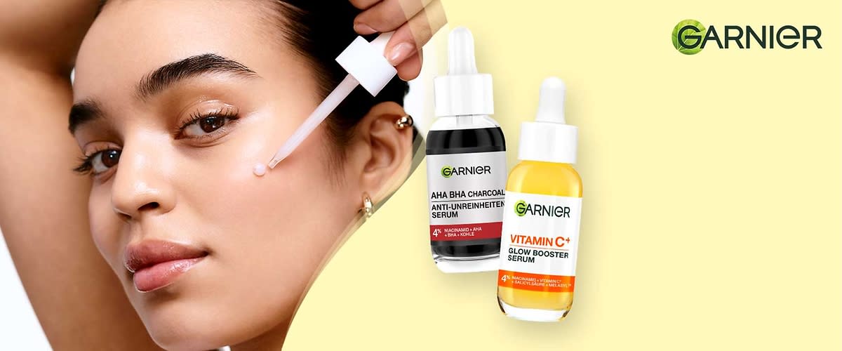 Zwei Garnier-Serumfläschchen mit Pipetten: links schwarzes Fläschchen mit Aufschrift „AHA BHA CHARCOAL ANTI-UNREINHEITEN SERUM“, rechts gelbes Fläschchen mit Aufschrift „VITAMIN C+ GLOW BOOSTER SERUM“, oben rechts Garnier-Logo