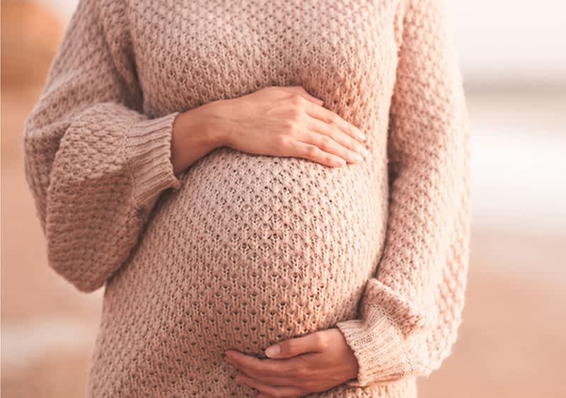 Schwangere Frau sitzt im Schneidersitz und fasst sich an den Bauch mit beiden Händen