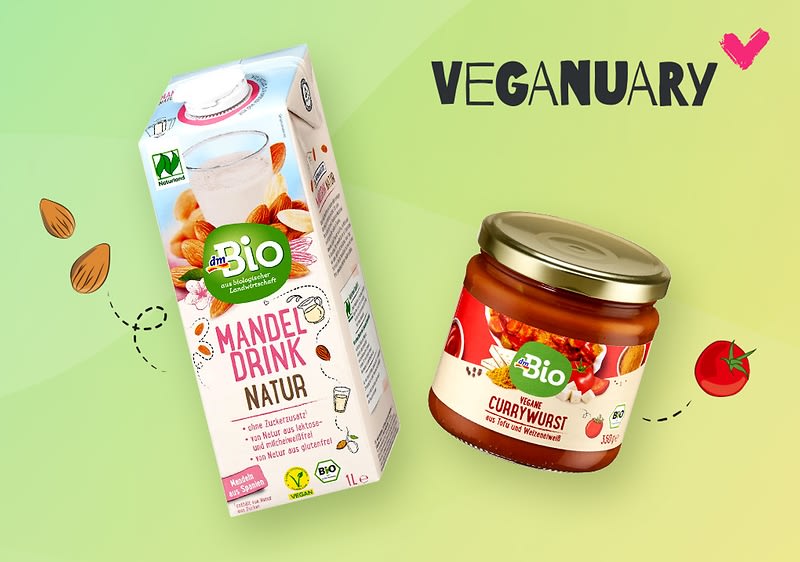Ein Tetrapak mit der Aufschrift „Bio Mandeldrink Natur“ und ein Glas mit der Aufschrift „Bio Vegane Currywurst“ auf einem grünen Hintergrund. Links sind gezeichnete Mandeln und rechts eine Tomate. Oben rechts steht „Veganuary“ mit einem pinken Herz.